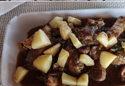 Fuente de carne de cabra guisada con salsa oscura y trozos de papa, servida en Casa Marcos