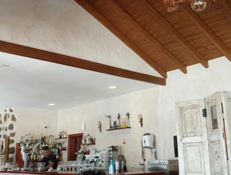 Barra del Restaurante Casa Marcos con techo de madera a dos aguas, botellas y cafetera; una persona trabajando detrás