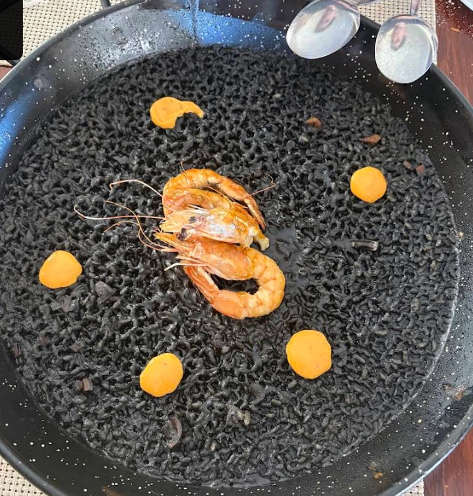 Paella de arroz negro con langostinos enteros y puntos de salsa anaranjada