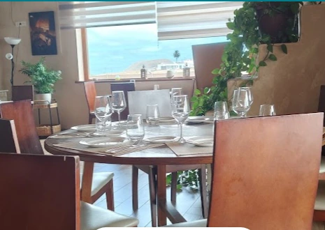 Comedor de Casa Marcos con mesas puestas, copas y plantas, junto a un ventanal con vistas al paisaje de Villaverde